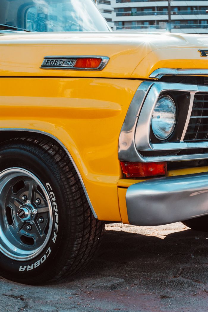 Detailed view of a vibrant yellow vintage Ford truck showcasing chrome front and tire.