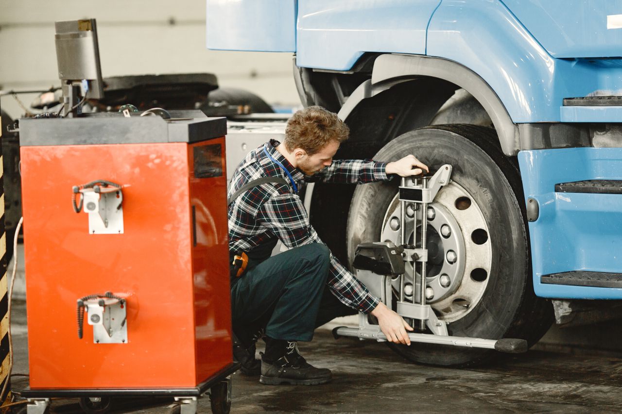 Mechanic performing tire alignment on a truck in an indoor workshop setting.